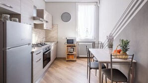 Una cocina moderna con horno empotrado, microondas y refrigerador de acero inoxidable. Hay una mesa de comedor con sillas y una cesta de fruta.