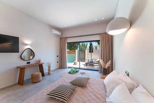 A modern bedroom with a bed, a bedside table, a mirror, and a view of an outdoor pool area.
