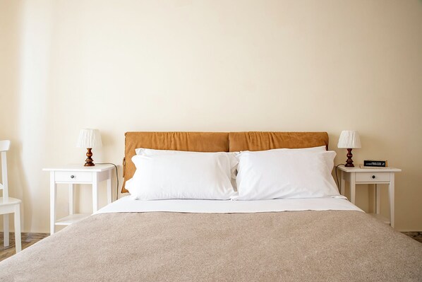A neatly made bed with white linens and a beige blanket, flanked by two bedside tables with lamps and books. - Ortigia Seafront Apartment by Wonderful Italy (Syracuse)