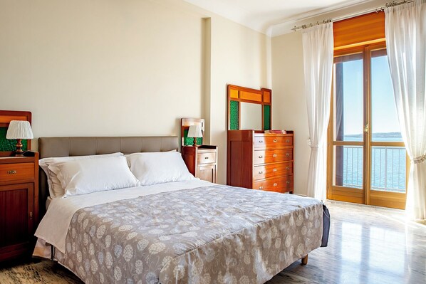 A bedroom with a bed, a dresser, a nightstand, and a window with curtains. - Ortigia Seafront Apartment by Wonderful Italy (Syracuse)