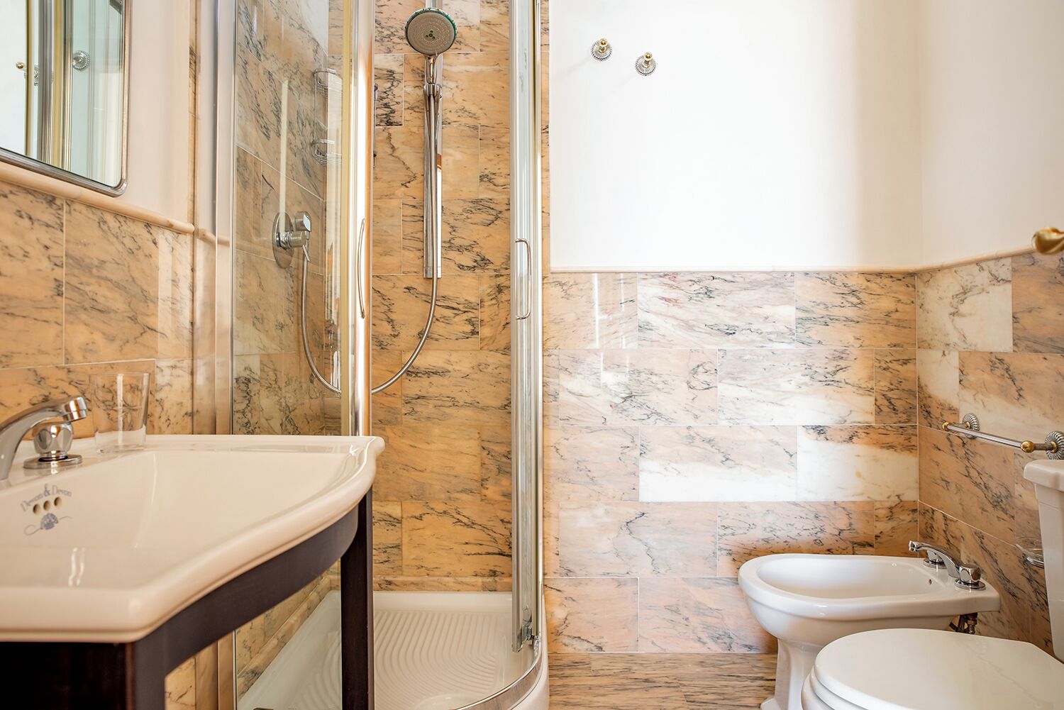 Ein Badezimmer mit Dusche, Toilette und Waschbecken, alles mit Marmorboden und -armaturen.
