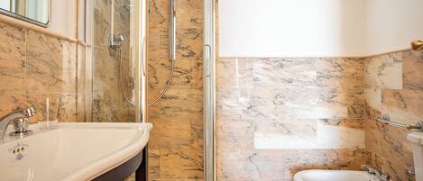 Ein Badezimmer mit Dusche, Toilette und Waschbecken, alles mit Marmorboden und -armaturen.