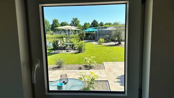 Uitzicht door een raam op een terras met een tafel en stoelen, een kleine tuin en een vijver.
