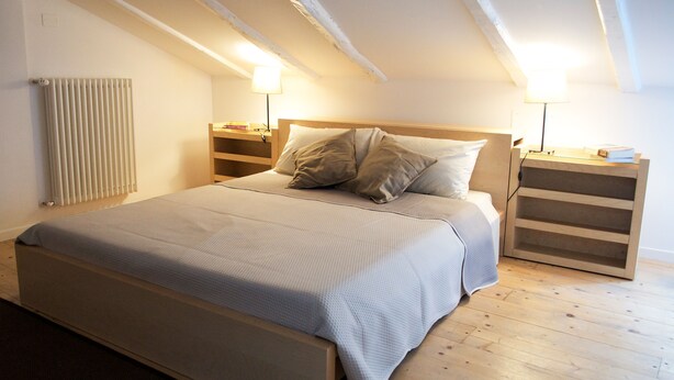A bedroom with a bed, wooden headboard, bedside tables, and a radiator. - Via de' Falegnami 6 Apartment by Wonderful Italy (Bologna)