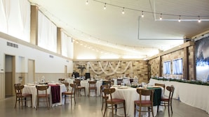 A banquet hall with round tables, chairs, and string lights.