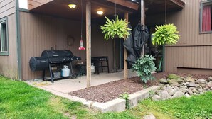 A covered patio area with a barbecue grill, outdoor table, and potted plants.