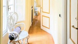 Un pasillo con una silla blanca, una puerta con un cartel y un suelo de baldosas.