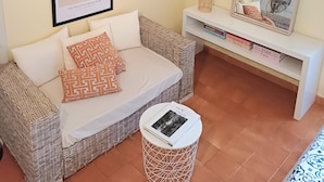 Una sala de estar acogedora con un sofá de mimbre, una mesita redonda, una obra de arte enmarcada, un espejo y una estantería con libros.