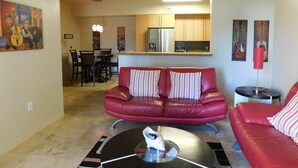 Un espace de vie compact comprenant un canapé en cuir rouge, un coin repas avec des chaises, une cuisine avec des meubles en bois et une petite table surmontée d’une lampe rouge.