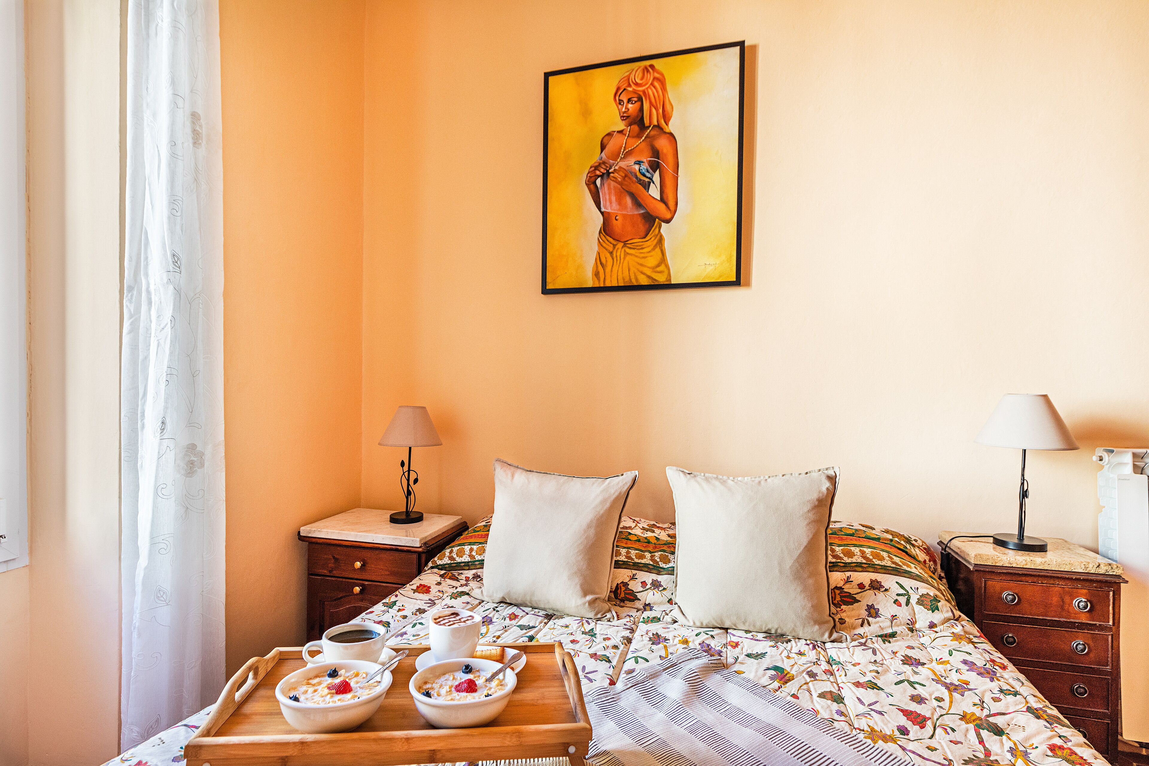 Une chambre à coucher avec un lit, des oreillers, une table de chevet avec une lampe, un plateau contenant des éléments pour le petit-déjeuner et un tableau accroché au mur.