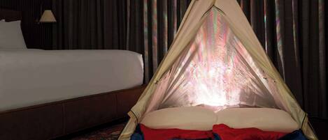 Habitación de hotel con una cama, una colcha roja y azul, y una tienda tipi con el logo de una montaña.