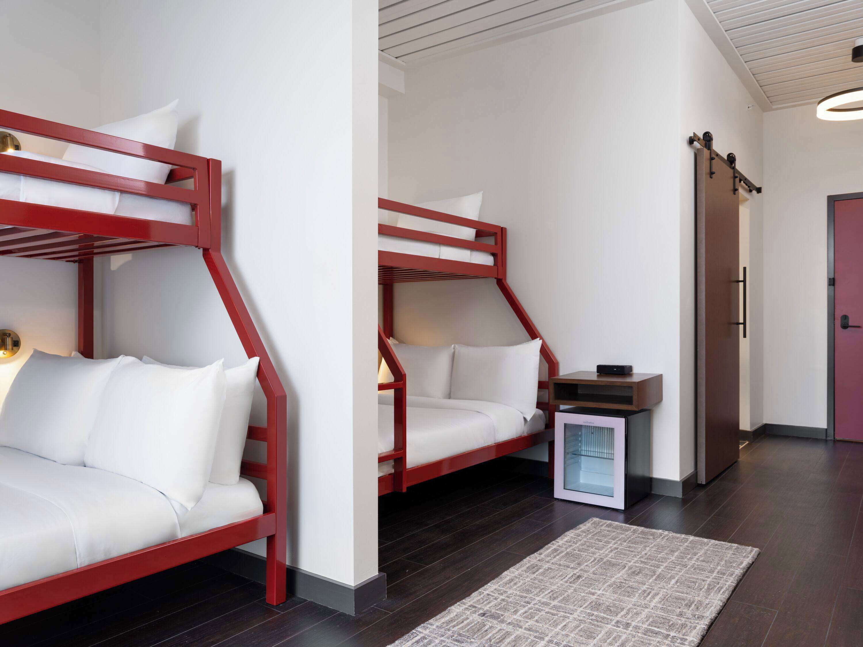 Ein modernes Hotelzimmer mit zwei Etagenbetten, einem kleinen Nachttisch, einer Glastruhe und einer Tür.