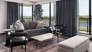 Una sala de estar moderna con un sofá gris, sillones de cuero negro, una mesa de centro y un ventanal con vistas a una masa de agua.