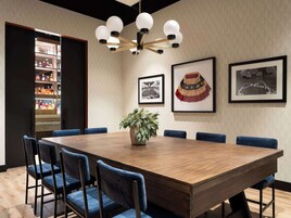 Un salón de conferencias con una mesa de madera, sillas azules, una planta en maceta y una araña.