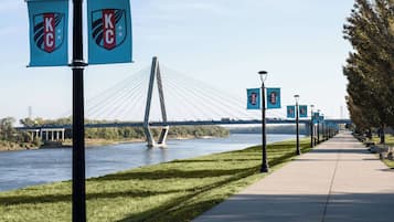 Une promenade piétonne bordée d’une rivière, d’un pont et de lampadaires ornés des logos de KC.