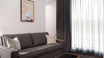 A modern living room with a grey sofa, a small black coffee table, and a large window with sheer curtains.