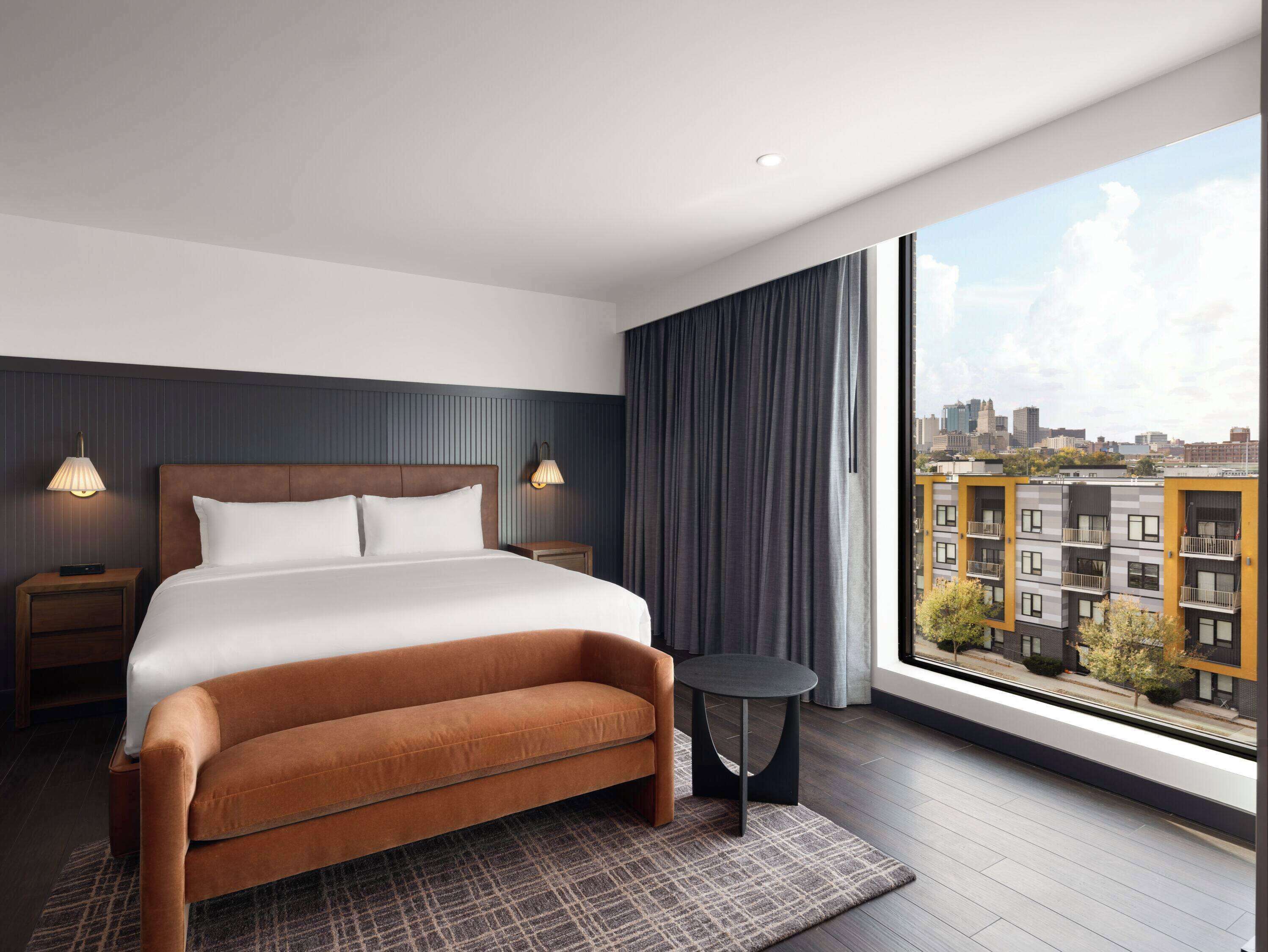 Habitación de hotel moderna con una cama grande, un sofá pequeño, una mesa redonda y vistas a la ciudad.