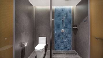 A modern bathroom with a toilet, a shower with a blue patterned wall, and a small shelf with toiletries.