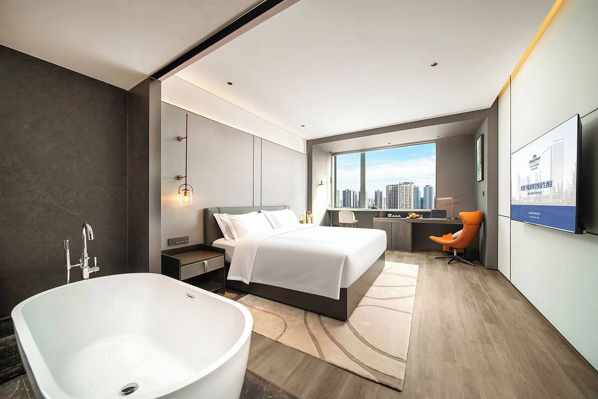 Una habitación de hotel moderna con una cama grande, una bañera, un escritorio y vistas a la ciudad.