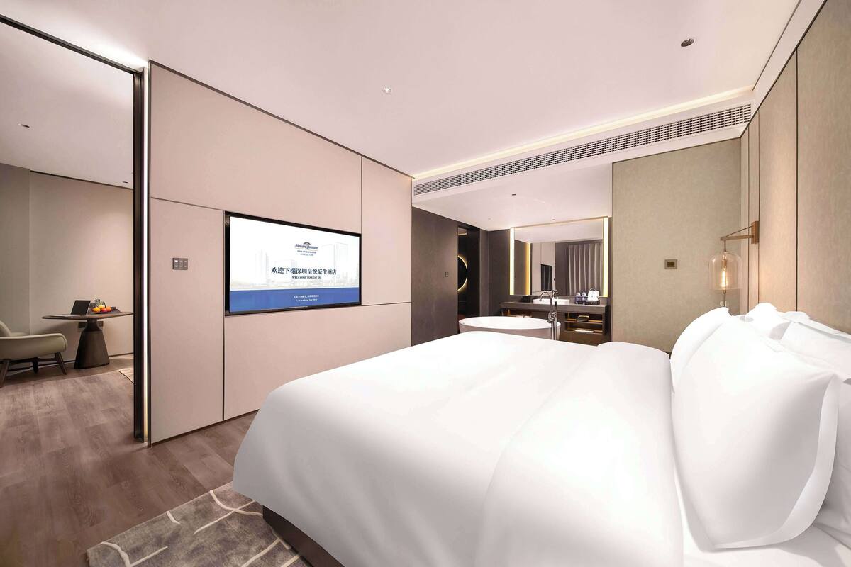 Habitación de hotel moderna con una cama grande, un escritorio con una silla, un televisor de pantalla plana y un baño con espejo y lavamanos.