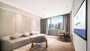 A modern living room with a sofa, a coffee table, and a view of the city skyline through large windows. - Howard Johnson Royal Hotel Shenzhen (Shenzhen)