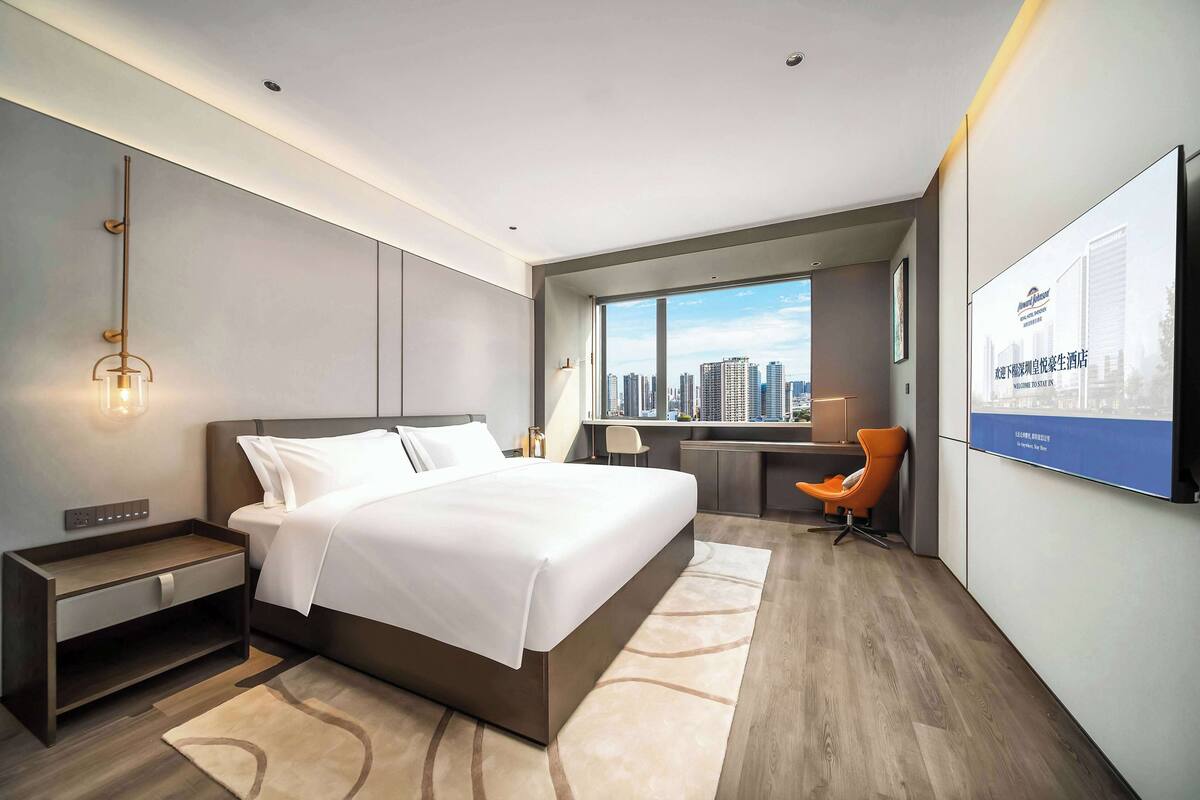 Una habitación de hotel moderna con una cama grande, un escritorio y vistas a la silueta urbana.