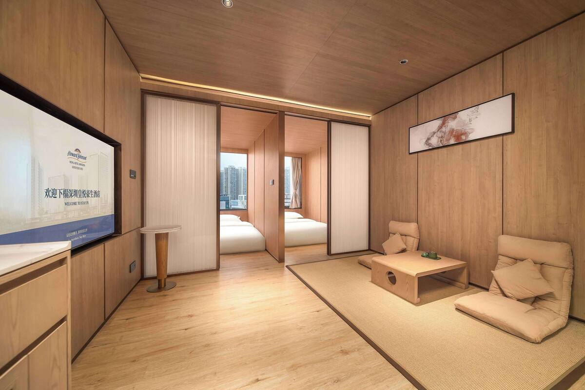 Habitación de hotel moderna con suelo de madera, cama, sofá, una mesita y televisor montado en la pared.