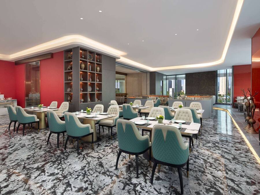 A modern dining area with marble flooring, teal chairs, and a central bar area.
