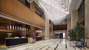 A spacious lobby with a reception desk, potted plants, and a modern ceiling design. - Wingate by Wyndham Urumqi Railway Station (Ürümqi)