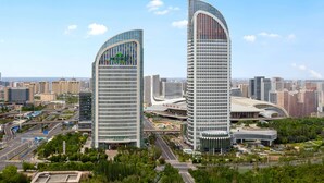 Two modern skyscrapers with curved glass facades, surrounded by a cityscape with other high-rise buildings. - Wingate by Wyndham Urumqi Railway Station (Ürümqi)