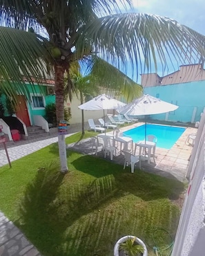 A backyard with a swimming pool, white lounge chairs, and umbrellas. - pousada maceio (Maceió)