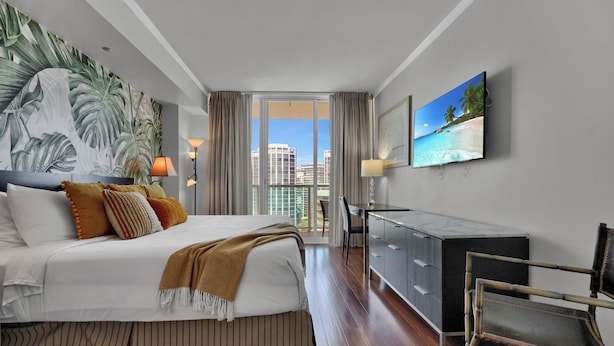 A modern hotel room with a large bed, a desk, a chair, a TV, and a balcony with a city view. - Spectacular Bay View 1bd 2baths in Grove (Miami)
