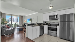 A modern kitchen with white cabinets, stainless steel appliances, and a large window offering a city view. - Spectacular Bay View 1bd 2baths in Grove (Miami)