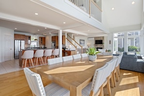 A spacious dining area with a wooden table and chairs, a kitchen in the background, and a staircase leading to an upper level. - Spacious York Home with Ocean Views & Hot Tub (York)