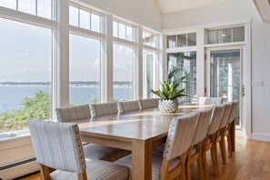 A dining area with a large table and chairs, a potted plant, and a view of the water. - Spacious York Home with Ocean Views & Hot Tub (York)