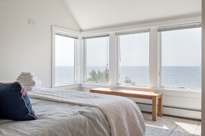 A bedroom with a bed, a bench, and a view of the sea through large windows. - Spacious York Home with Ocean Views & Hot Tub (York)