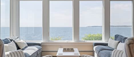 A room with a large window overlooking the sea, featuring a sofa and a small table.