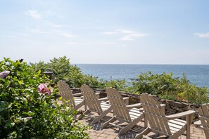 A row of wooden Adirondack chairs facing a body of water, with greenery and a clear sky in the background. - Spacious York Home with Ocean Views & Hot Tub (York)