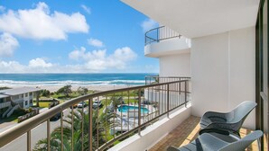 A balcony with a view of the ocean, a pool, and outdoor seating.