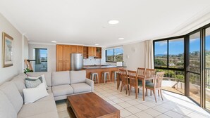 A modern apartment with a living room, kitchen, and dining area. It features a large window with a view of the city.