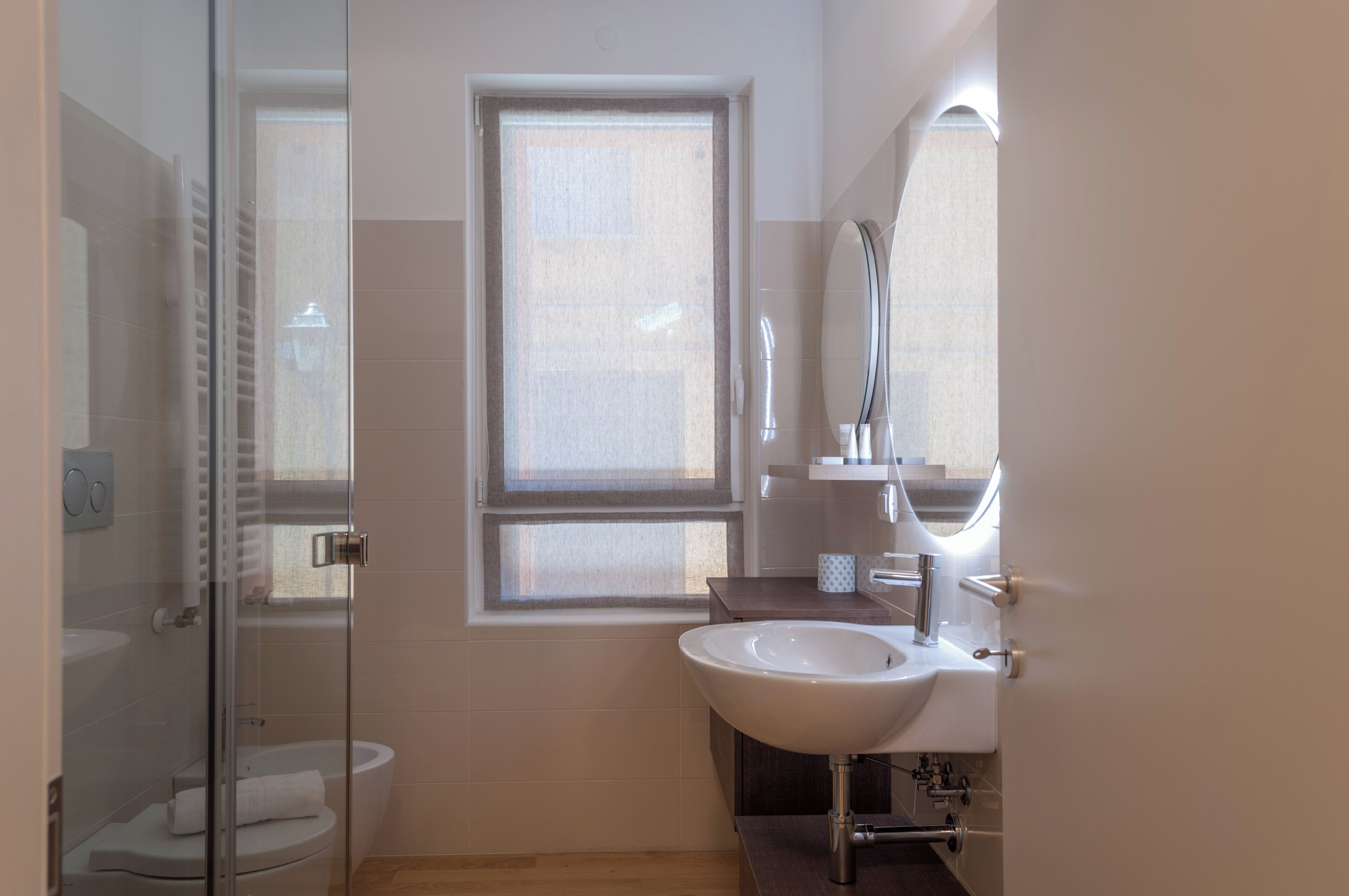 Ein modernes Badezimmer mit Duschkabine aus Glas, Toilette, Waschbecken und einem Fenster für natürliches Licht.