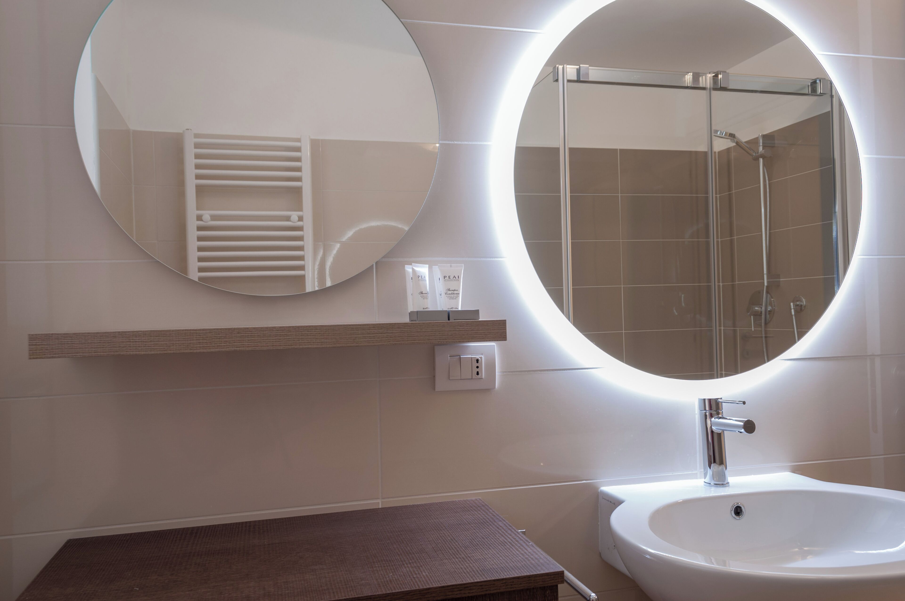 A bathroom with a round mirror, a sink, and a shower.