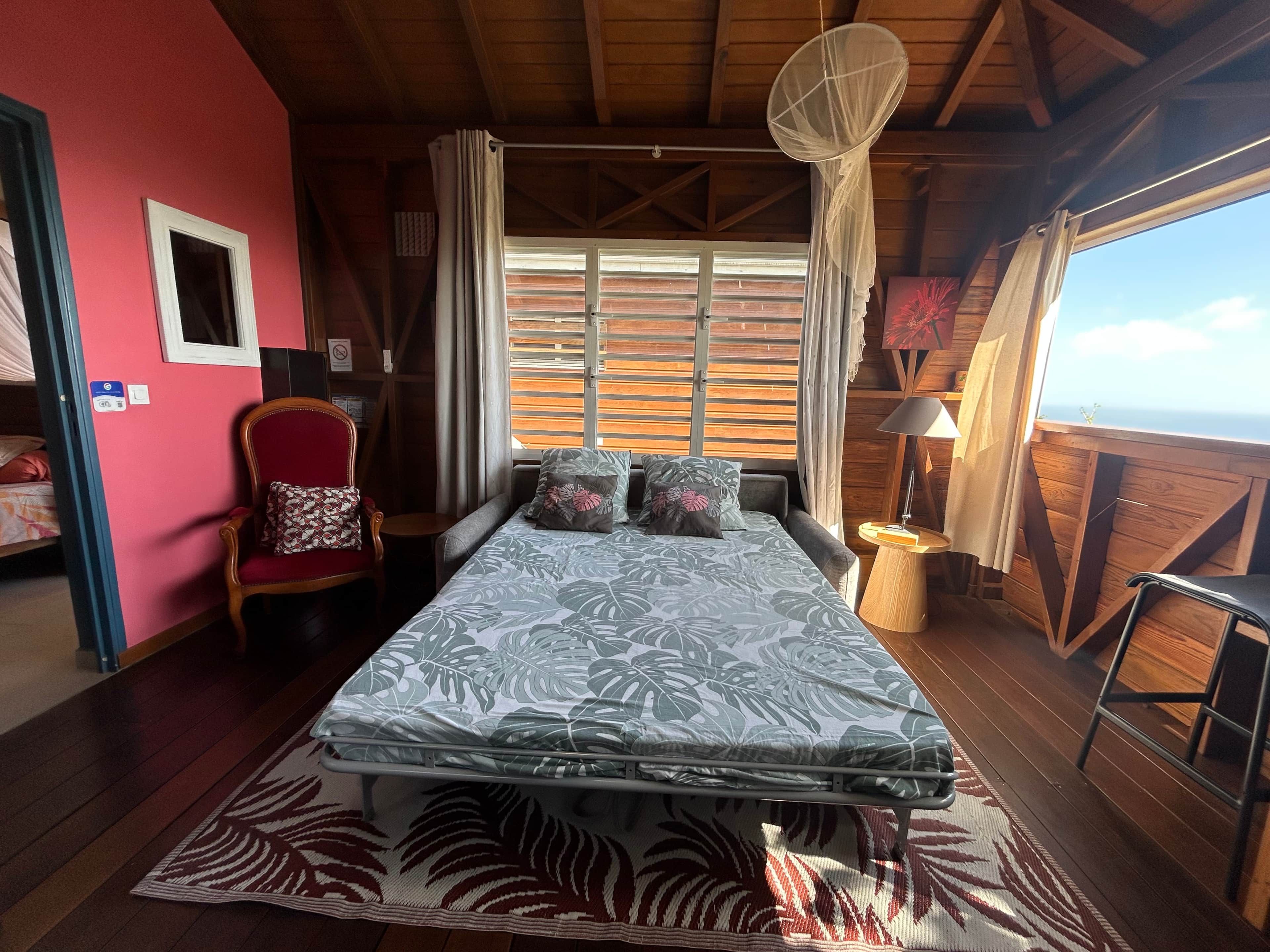 Una habitación con cama, una silla, ventana con cortinas y vistas al exterior.