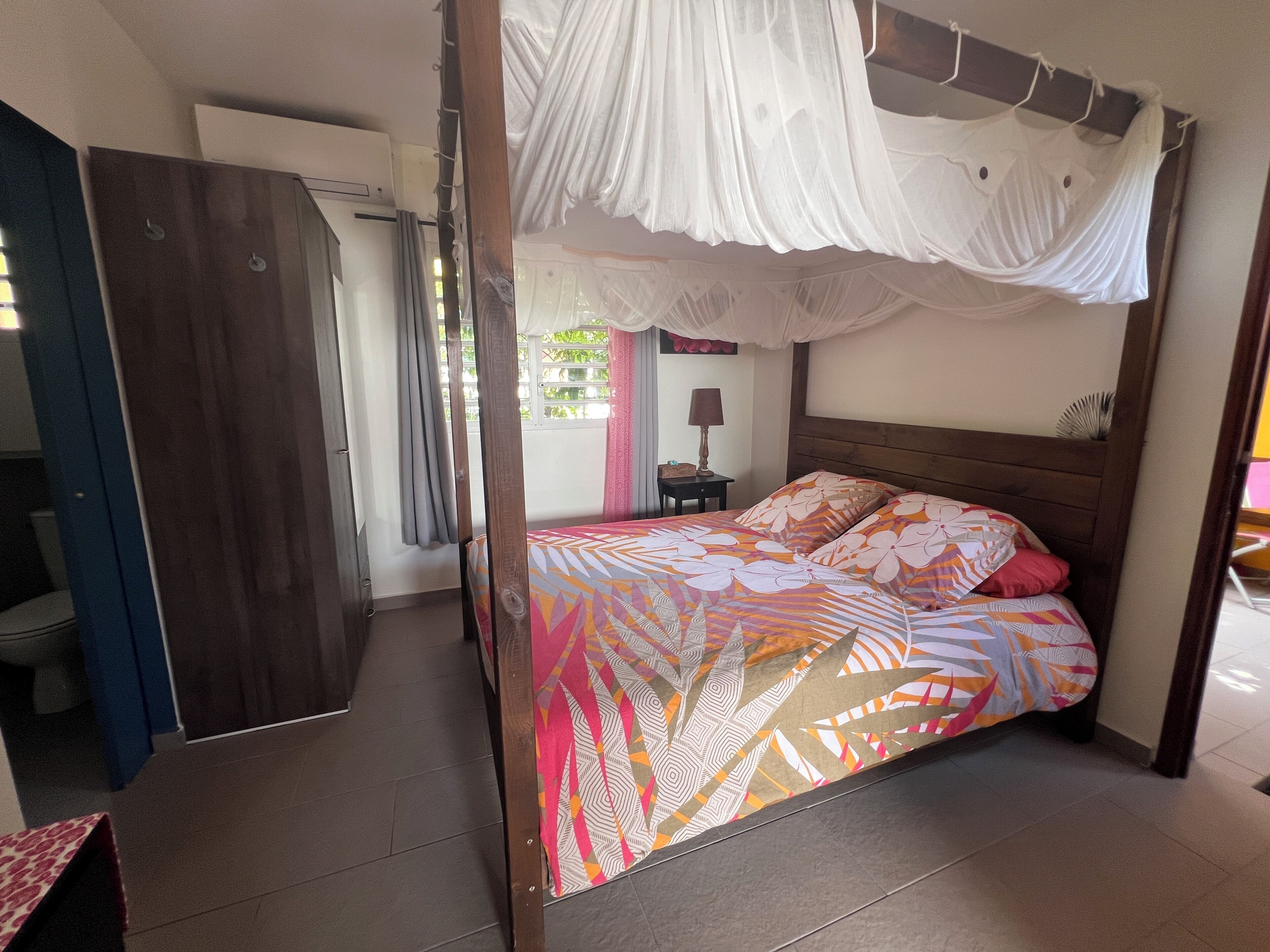 Un dormitorio con una cama con dosel, un armario de madera y una mesita de noche con una lámpara.