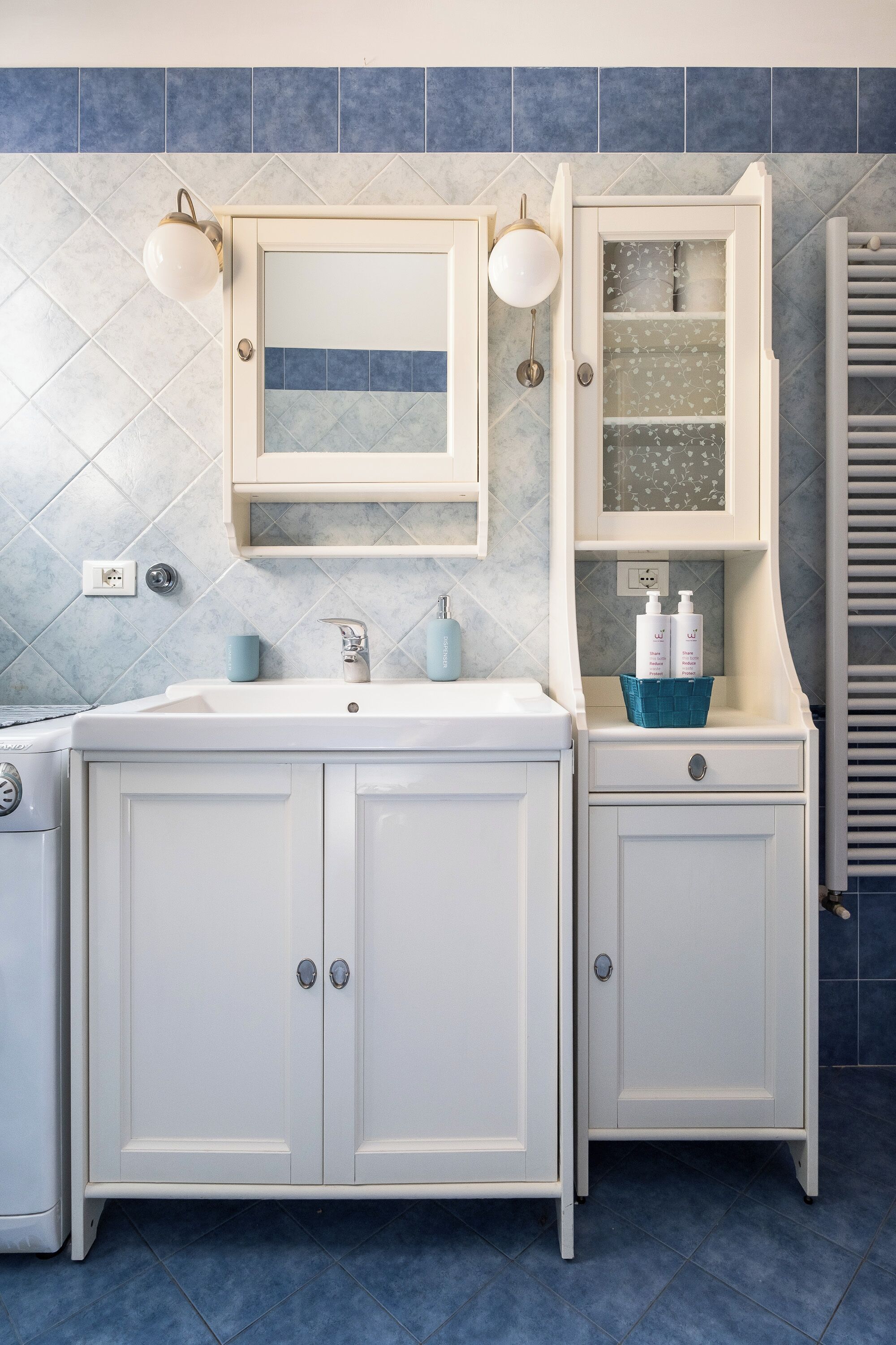 Un baño con tocador blanco, espejo y mueble con artículos de aseo.