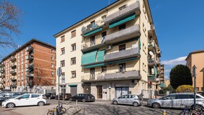A multi-story residential building with balconies, a parking area, and a clear blue sky. - San Donato Cozy Apartment by Wonderful Italy (Bologna)