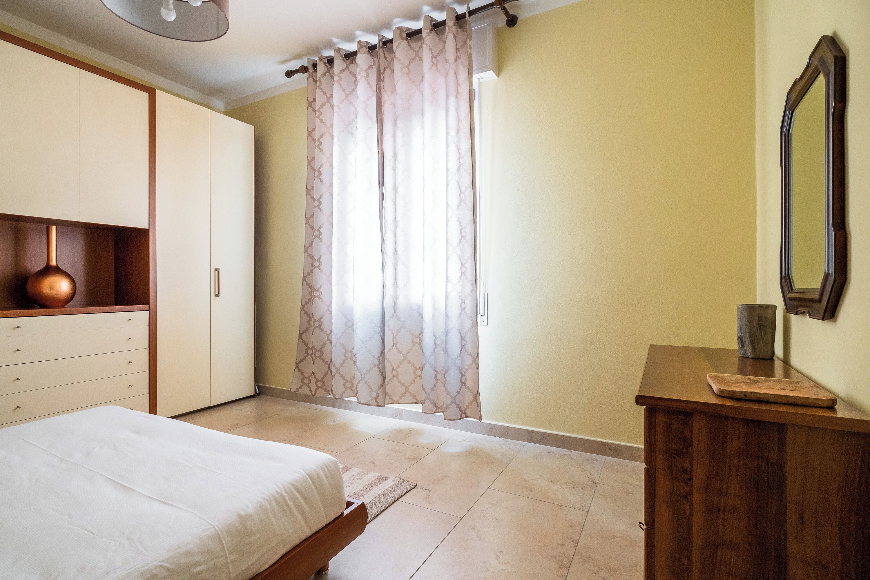 Un dormitorio con cama, armario, espejo y cómoda de madera.