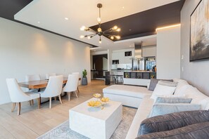 Een moderne woonkamer met een eethoek, een zithoek, een salontafel en een keuken op de achtergrond.