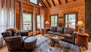 A cozy cabin interior with a leather sofa, a wooden coffee table, and a fireplace.