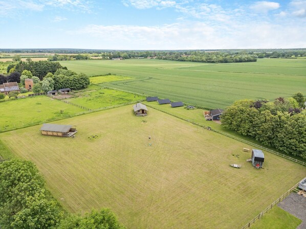 Vista aérea de una propiedad rural con varias construcciones agrícolas, campos abiertos y una amplia zona verde.